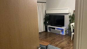 A living room with a flat-screen TV on a white stand, a wooden chair, a small table, and a potted plant. - Charming 2-bed Apartment in Bow, London (London)