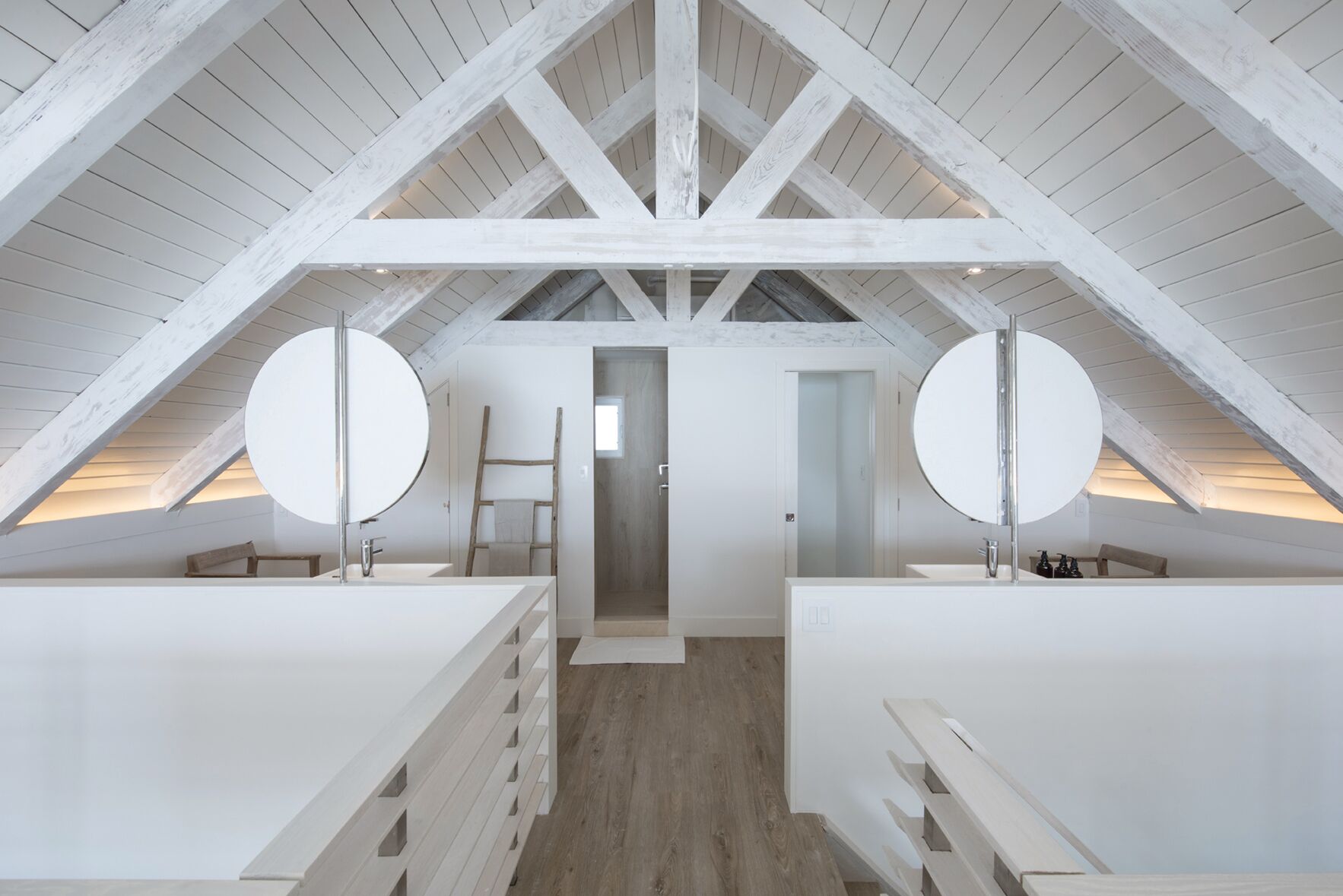 A modern attic bedroom with white wooden beams, two large round mirrors, and a wooden ladder.