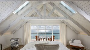 Ein Schlafzimmer mit einem großen Bett, Meerblick und einer hohen Decke mit freiliegenden Balken.