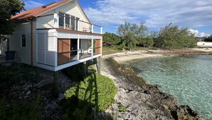 Ein zweistöckiges Haus mit einem Balkon mit Blick auf einen Strand und klares Wasser.