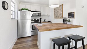 A modern kitchen with white cabinets, stainless steel appliances, a wooden island with stools, and a decorative wall piece. - Walking on Sunshine – 2BR, 1BA Near Riverwalk (Fort Lauderdale)