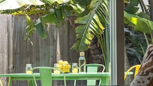 A green metal table with chairs, a wooden fence, and banana plants in the background. - Walking on Sunshine – 2BR, 1BA Near Riverwalk (Fort Lauderdale)