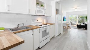 A modern kitchen with white cabinetry, a built-in microwave, and a stove. There is a dining area with a table and chairs visible in the background. - Private 2 Bedroom Apartment Near Beach (Fort Lauderdale)