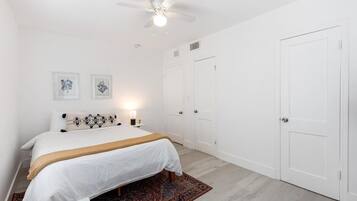A bedroom with a bed, a ceiling fan, two doors, and a nightstand with a lamp.