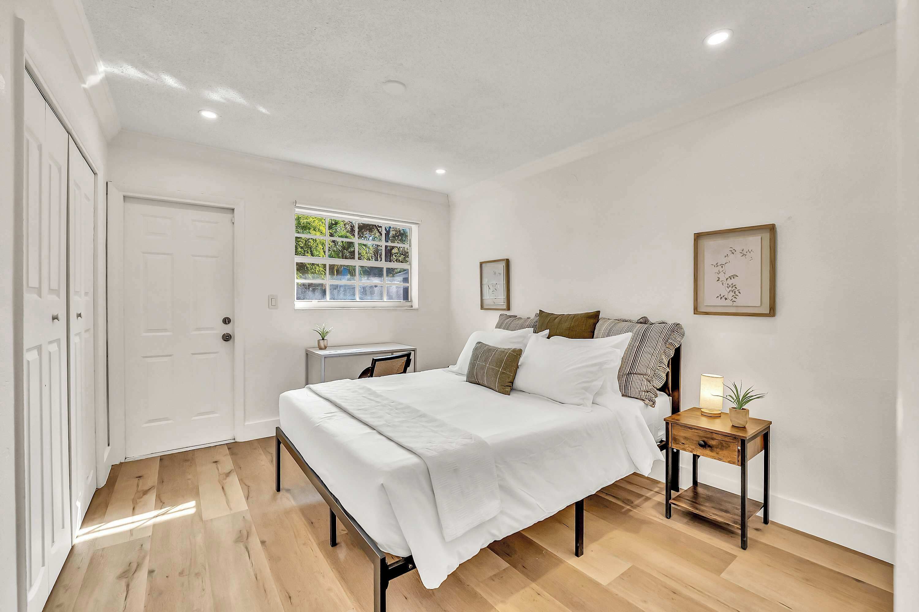 A bedroom with a bed, bedside table, window, and a door.