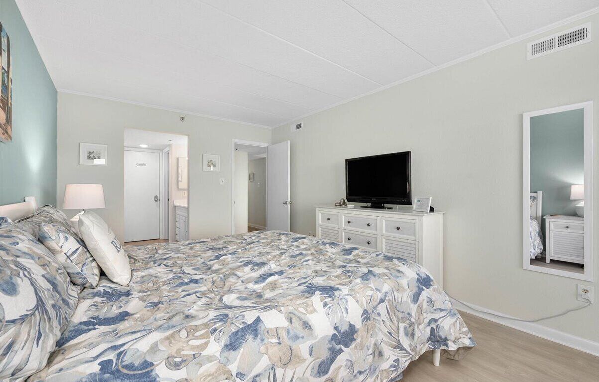 A bedroom with a large bed, a television, a dresser, and a mirror.