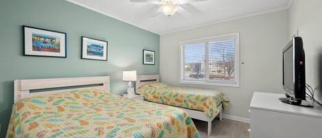 A bedroom with two beds, a ceiling fan, a TV, and framed pictures on the wall.
