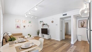 A modern living room with a dining area, white walls, wooden flooring, and a flat-screen TV. - Charming Waterfront Apartment – Las Olas Blvd Isle (Fort Lauderdale)