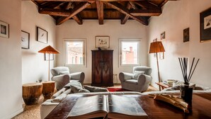 Une pièce chaleureuse avec un haut plafond en bois, deux fauteuils, un grand livre ouvert sur une table et un buffet au centre.