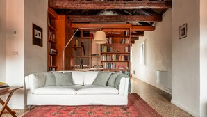 Un salon chaleureux avec un canapé blanc, un tapis rouge à motifs, des étagères en bois et un plafond en bois.