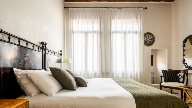 Un dormitorio con cabecera de madera, cama con ropa blanca, un plaid verde y una silla con cojín.