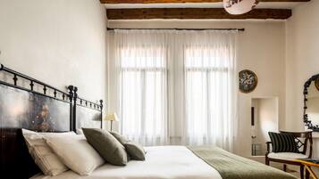 Un dormitorio con cabecera de madera, cama con ropa blanca, un plaid verde y una silla con cojín.