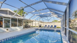 A covered swimming pool with a clear blue water surface, surrounded by lounge chairs and a patio area with a wooden fence in the background. - Pet-friendly Home w/ Heated Pool in Bradenton (Bradenton)