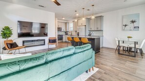 A modern living room with a green sofa, a flat-screen TV, and a ceiling fan. - Modern Pensacola Vacation Home w/ Private Pool! (Pensacola)