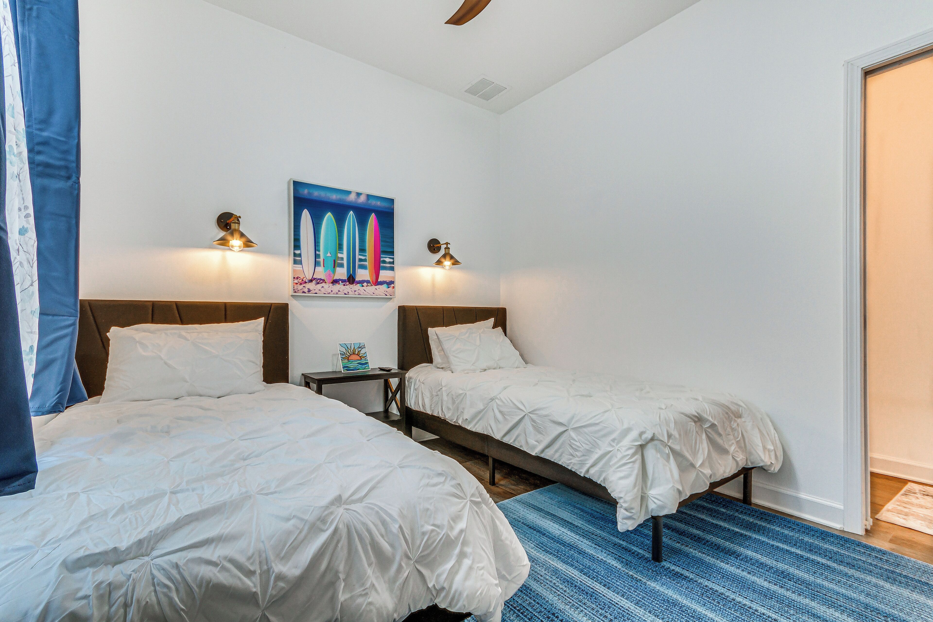 Een slaapkamer met twee bedden, een blauw vloerkleed en een schilderij aan de muur.