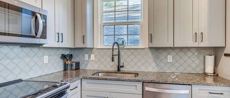 A modern kitchen with white cabinets, a stainless steel dishwasher, a built-in microwave, and a window with a view of the roof.