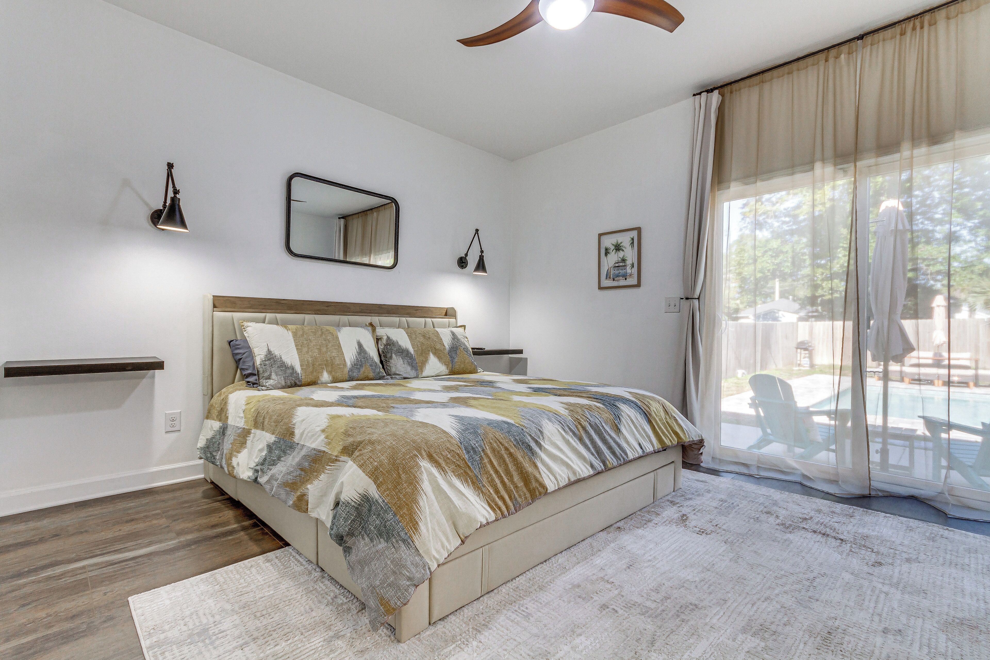 Een slaapkamer met een bed, nachtkastjes, een plafondventilator en uitzicht op een buitenzwembad.