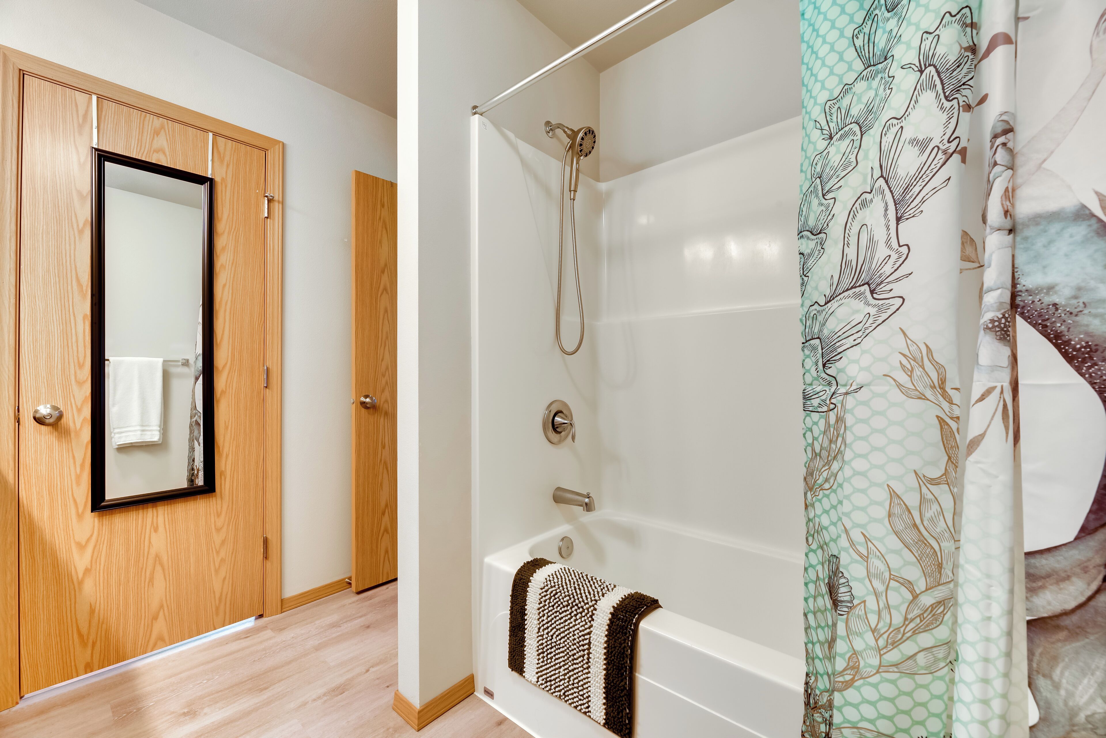 Une salle de bain avec une baignoire, une douche et une porte en bois dotée d’un miroir.
