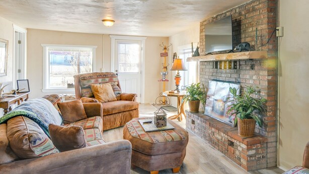 A cozy living room with a brick fireplace, comfortable seating, and a view of the outdoors. - Downtown Del Norte Home Near Hiking & Fishing! (Del Norte)