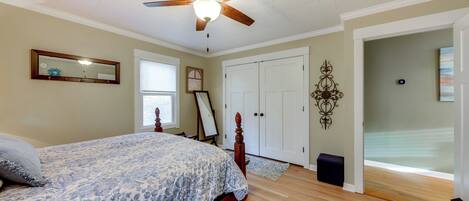 A bedroom with a bed, a ceiling fan, a wardrobe, and a door leading to another room.