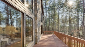 Eine Holzdielen-Terrasse mit einer Steinmauer und Glastüren, umgeben von einem Wald.