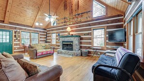 L’intérieur d’une cabane en rondins, avec une cheminée en pierre, un plancher en bois et un téléviseur.