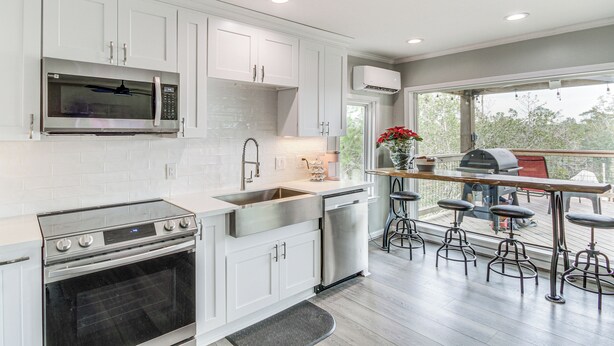 A modern kitchen with white cabinets, stainless steel appliances, a large window, and a deck area with bar stools. - Bay St Louis Home w/ Private Dock + Kayaks! (Bay St Louis)