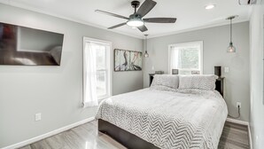 A bedroom with a bed, ceiling fan, artwork, and a window. - Bay St Louis Home w/ Private Dock + Kayaks! (Bay St Louis)