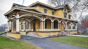 A two-story yellow house with a porch, a front entrance, and a flag. - Historic Chambersburg Home w/ Pool + Game Rooms! (Chambersburg)