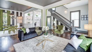 A spacious living room with a dark-colored sofa, a glass coffee table, and a staircase leading to another level. - Stylish Home in Springfield Historic District! (Jacksonville)