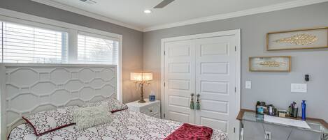 A bedroom with a bed, a nightstand, a desk, a ceiling fan, and a door.