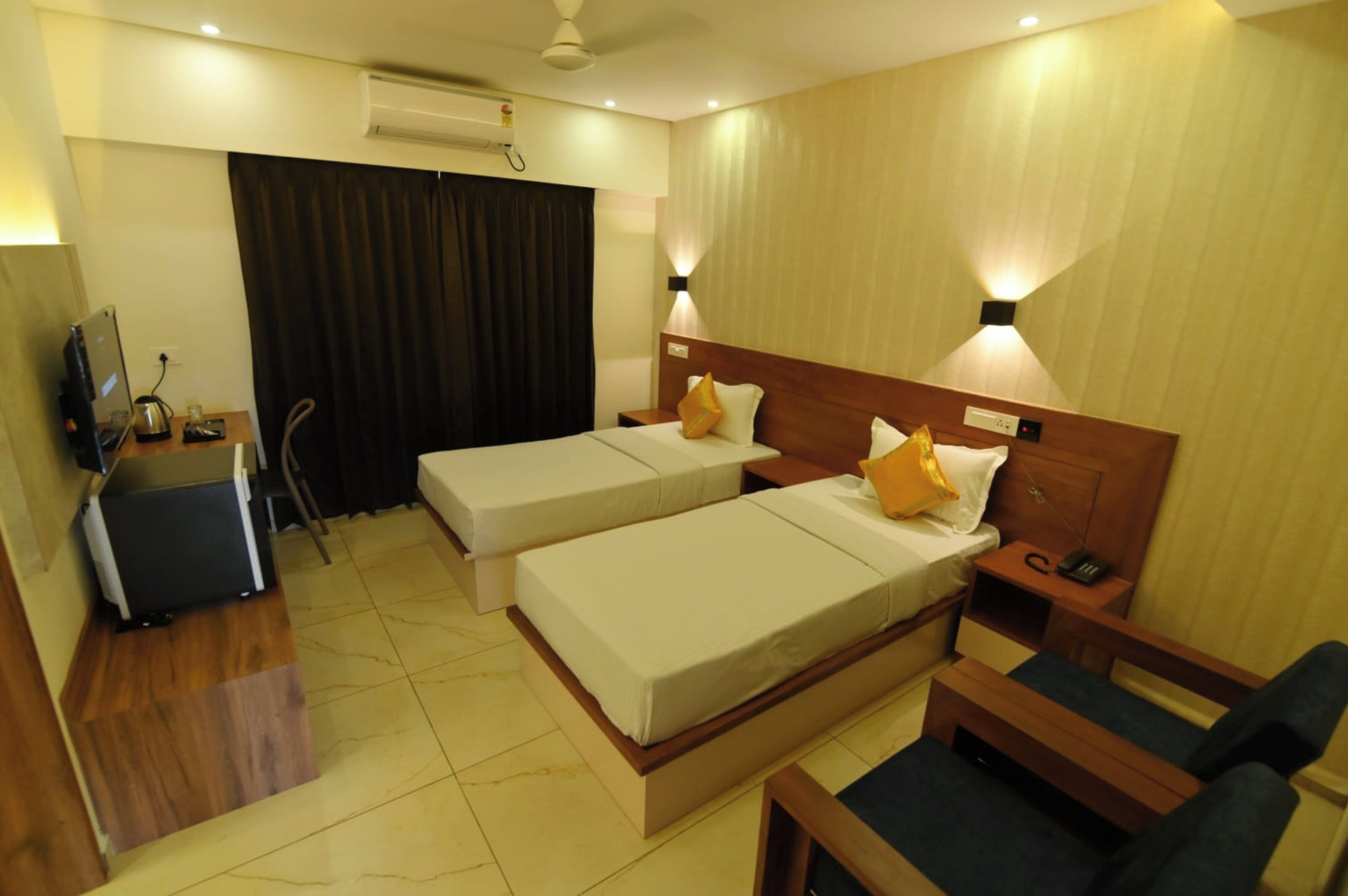 A hotel room with two single beds, a desk with a chair, a small sofa, and a TV.