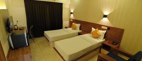 A hotel room with two single beds, a desk with a chair, a small sofa, and a TV.