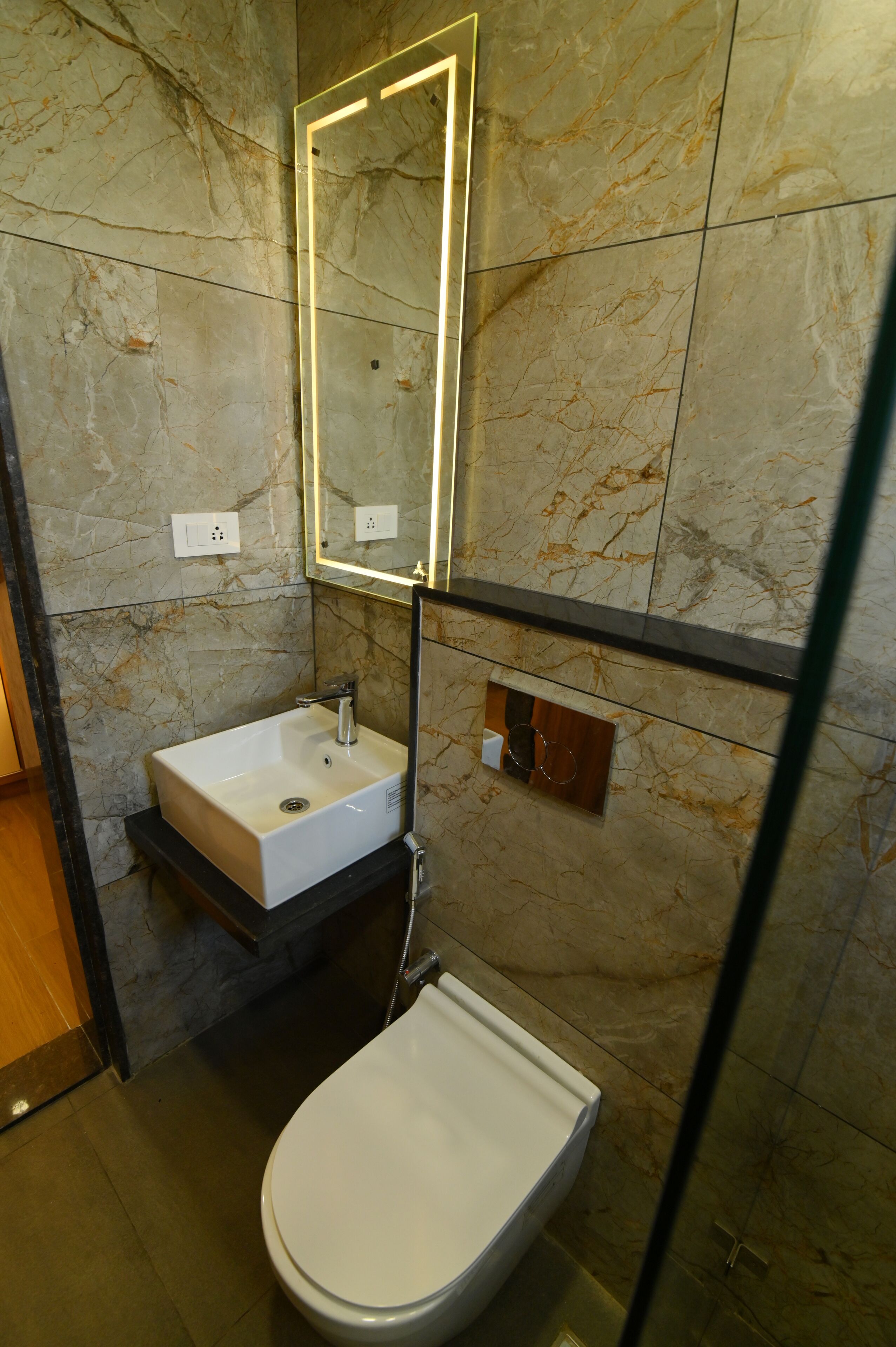 A bathroom with a marble wall, a white sink, a mirror, and a toilet.
