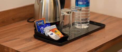 A tray with a kettle, a bottle of water, and packets of tea and coffee on a wooden table.