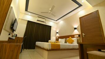 Ein Hotelzimmer mit Bett, Schreibtisch, Fernseher, Klimaanlage und Deckenventilator.