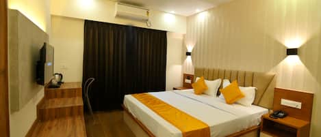 Una habitación de hotel con cama, mesitas de noche, televisor, escritorio y una silla.