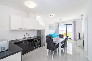 Una cocina moderna con armarios blancos, encimera negra y un comedor con mesa y sillas.