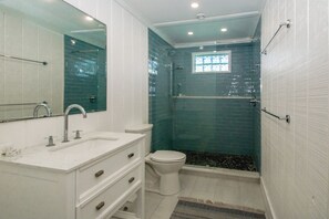 A bathroom with a white vanity, a toilet, a glass-enclosed shower, and a window.