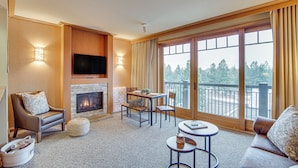 Amplia sala de estar con chimenea, asientos cómodos, televisor y ventanas grandes con vistas al exterior.