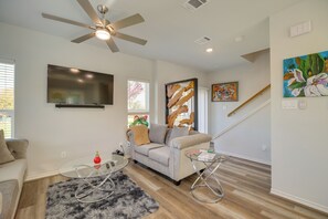 A modern living room with a ceiling fan, a flat-screen TV, a grey sofa, a glass coffee table, and a wooden floor. - South Houston Townhome w/ Patio & Gas Grill! (South Houston)