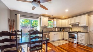 A modern kitchen with white cabinets, a built-in oven, and a dining area with a wooden table and chairs. - Devon Court 2 Bedroom Home by RedAwning (Hood River)