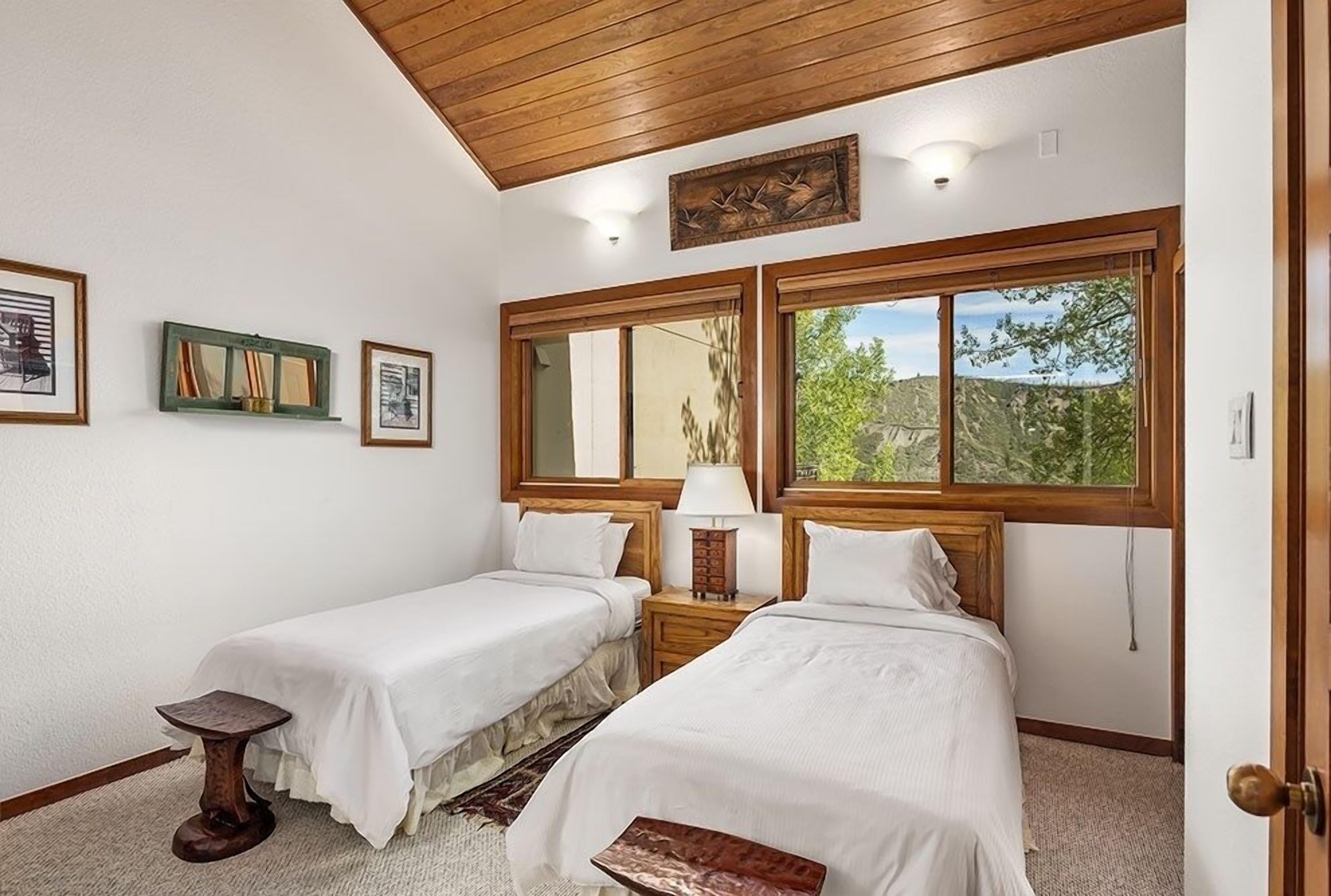 A room with two beds, a small table, and a window with a view of greenery.