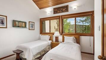 A room with two beds, a small table, and a window with a view of greenery.
