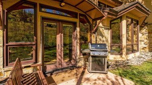 A covered patio with a grill, a bench, and a view of a stone building. - Townhome With Ski-in Access Near Pool And Spa by The Woodrun V Townhouses by RedAwning (Snowmass Village)