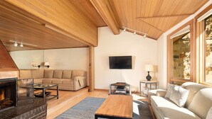 A living room with a fireplace, a sofa, a coffee table, and a TV mounted on the wall. - Townhome With Ski-in Access Near Pool And Spa by The Woodrun V Townhouses by RedAwning (Snowmass Village)