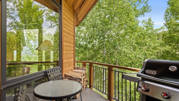 A wooden deck with a round table and chairs, a grill, and a view of trees. - Contemporary Townhome With Ski-in/ski-out Access by The Woodrun V Townhouses by RedAwning (Snowmass Village)