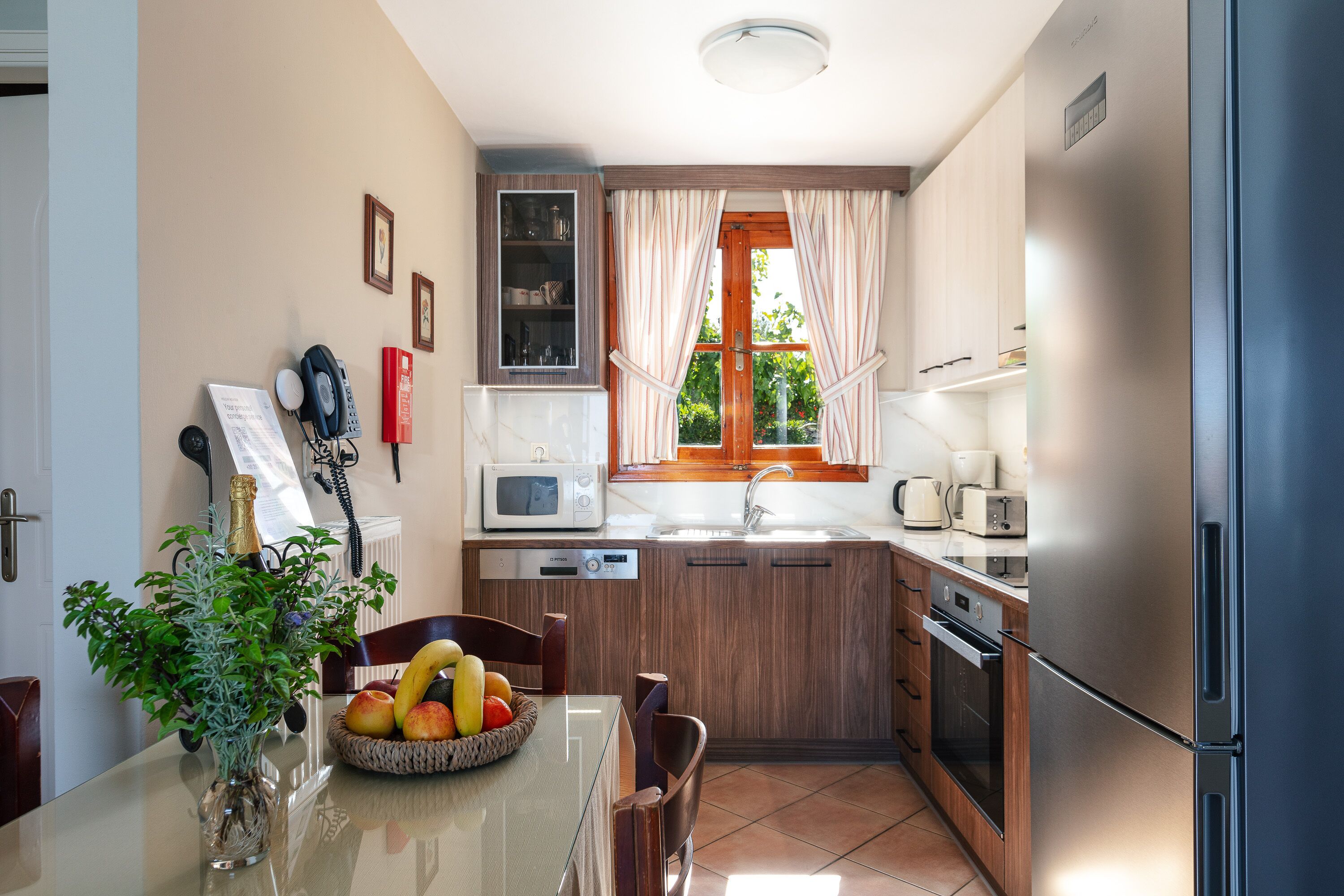 Una cucina compatta con mobili in legno, un frigorifero in acciaio inossidabile, un forno a microonde e un lavello. C'è un tavolo da pranzo con sedie e una ciotola di frutta.