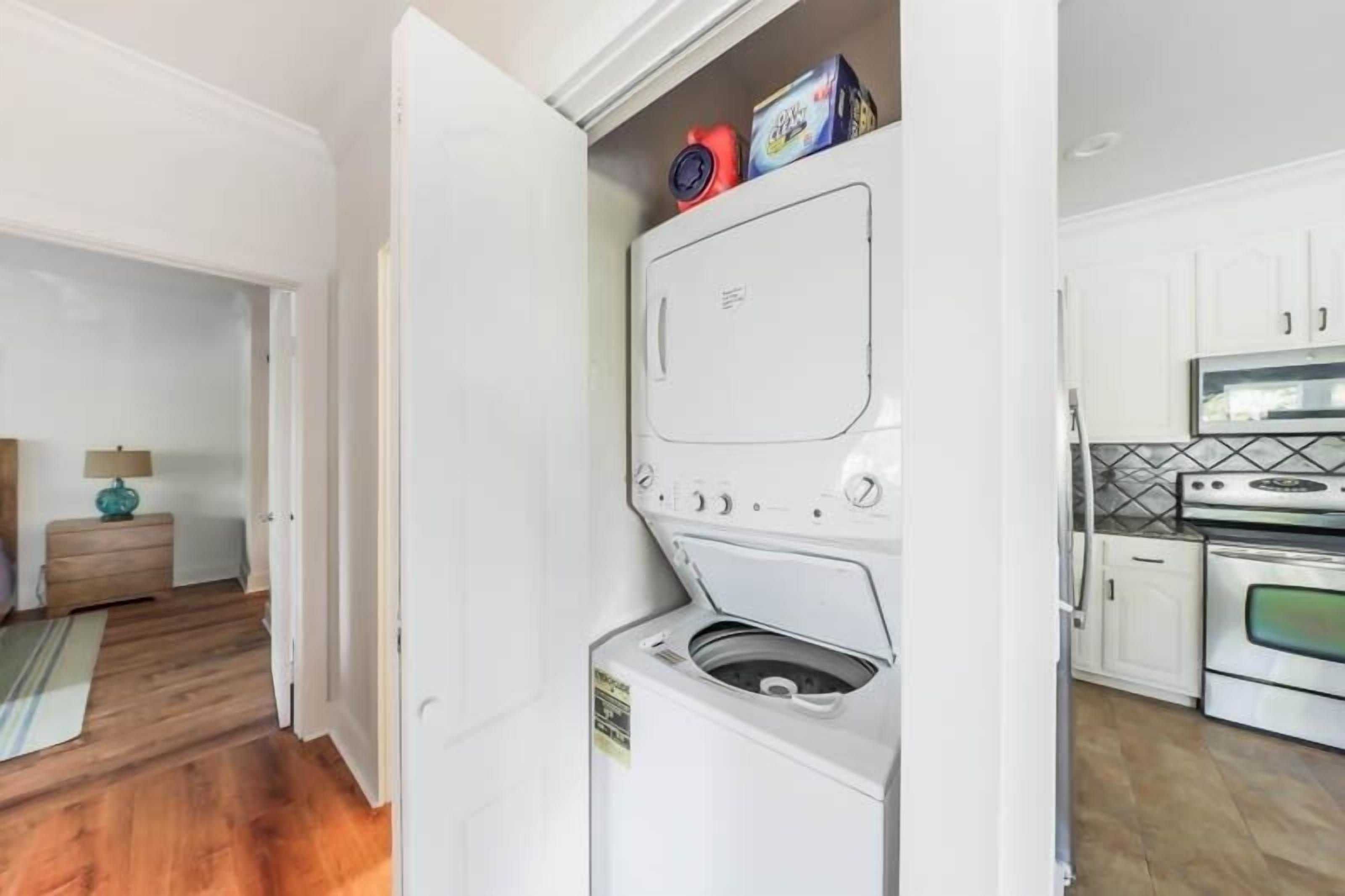 A laundry room with a washer and dryer, a small table with a lamp, and a kitchen area with cabinets and appliances.