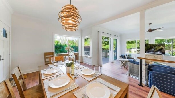 Un comedor con una mesa de madera dispuesta para cuatro, una lámpara colgante y vistas al exterior a través de amplios ventanales.